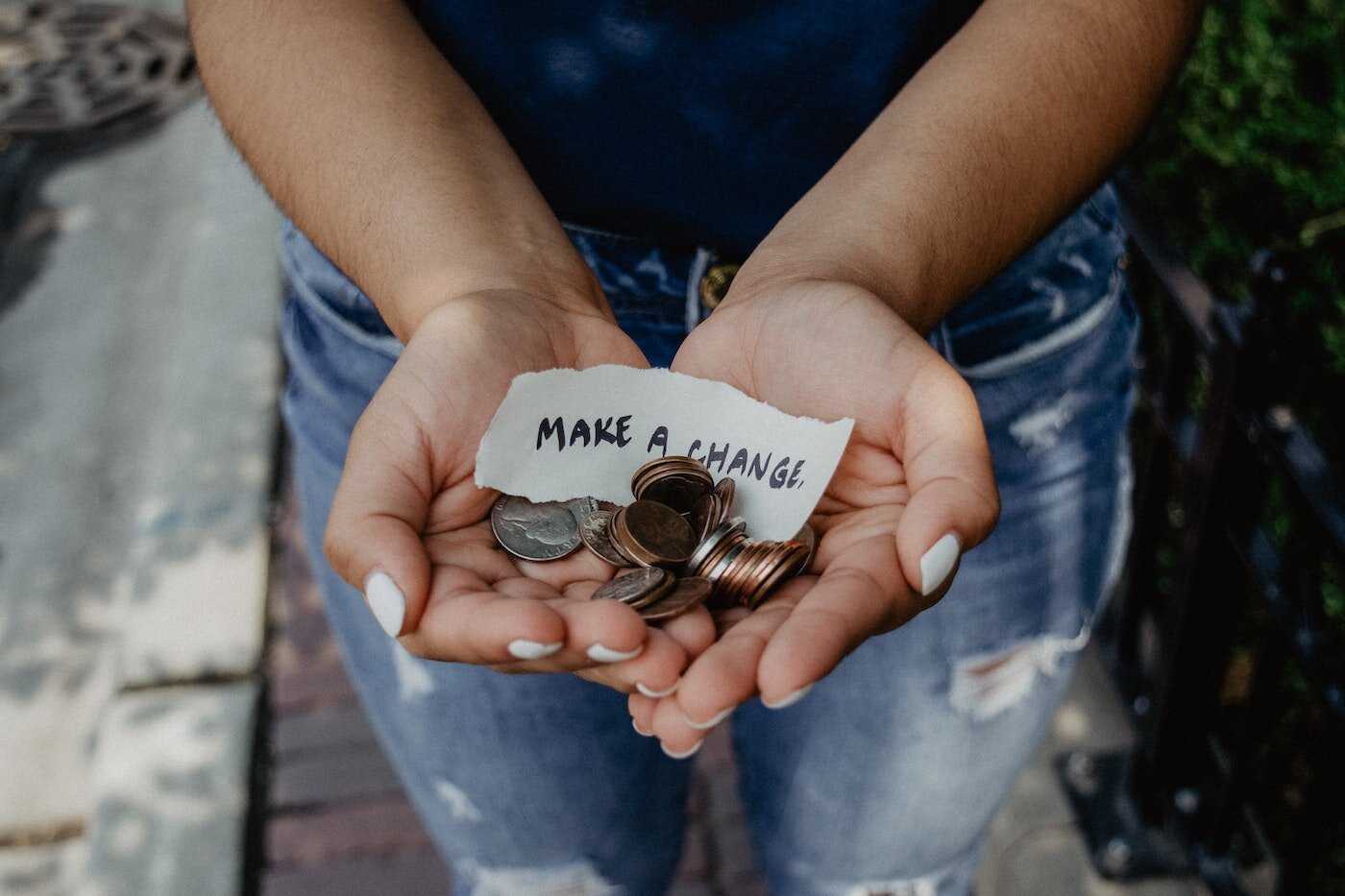 A woman with her hands held out with coins in her hands and a note that reads "make a change."