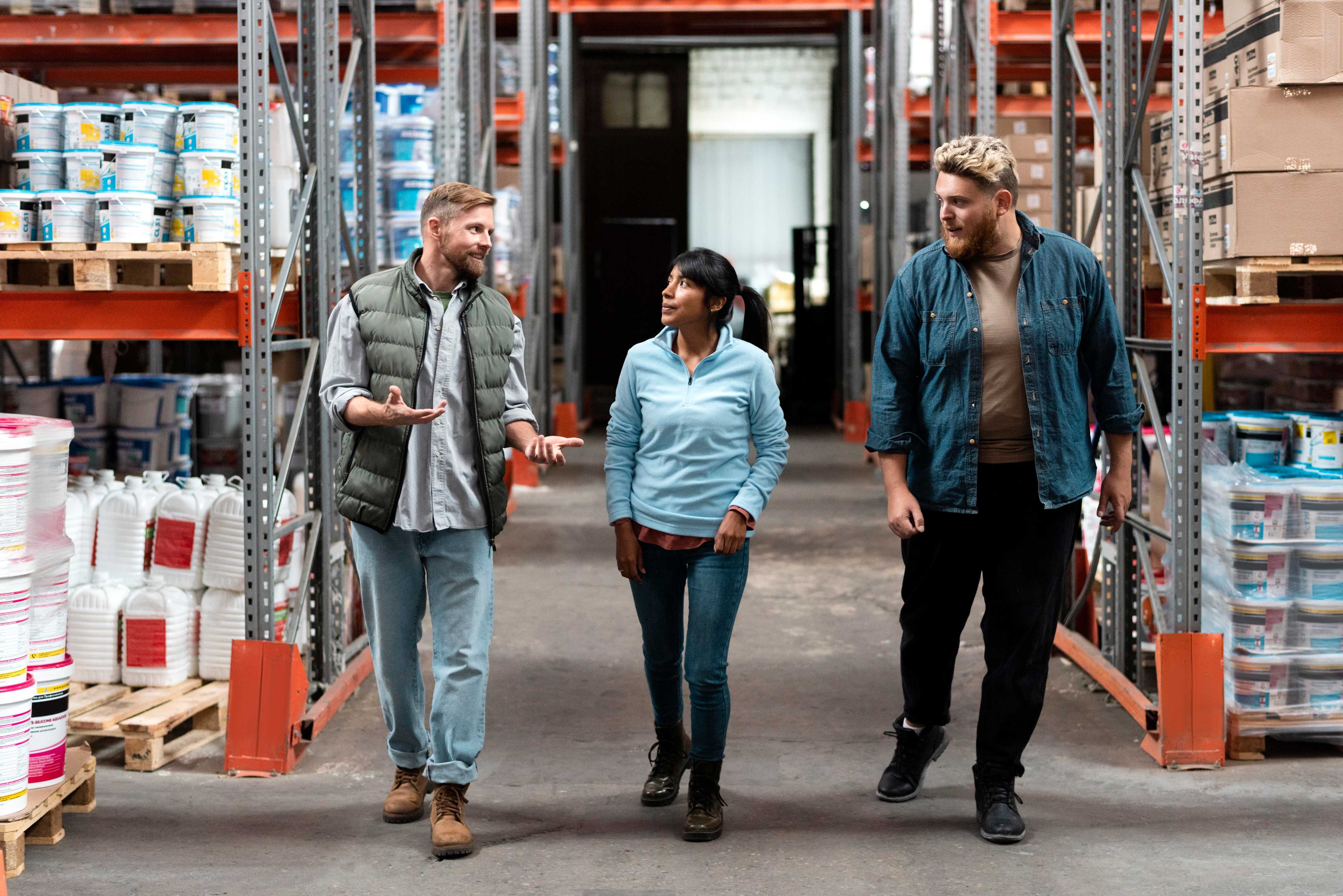 3 people walking through a warehouse having a conversation.